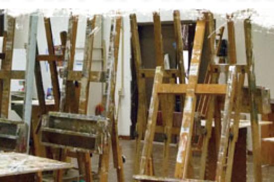 A person painting in a room full of empty easels marked with paint